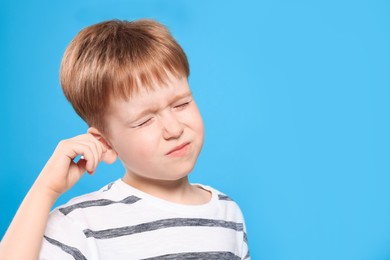 Photo of Little boy cleaning ear with cotton swab on light blue background. Space for text