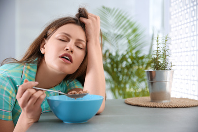 Photo of Sleepy young woman eating breakfast at home in morning