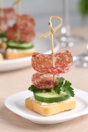 Photo of Tasty canapes with salami, cucumber and cream cheese on light table, closeup