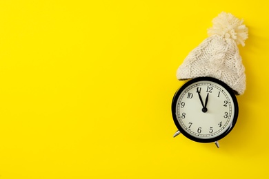 Photo of Alarm clock in hat on yellow background, top view with space for text. New Year countdown