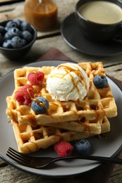 Delicious Belgian waffles with ice cream, berries and caramel sauce served on wooden table, closeup