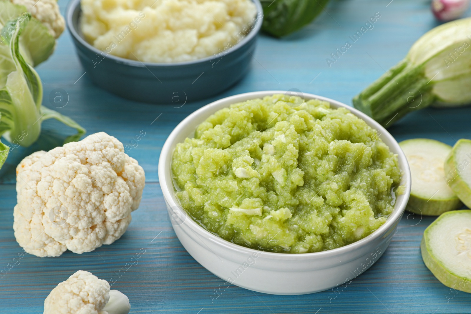 Photo of Tasty puree in bowls and ingredients on light blue wooden table, closeup