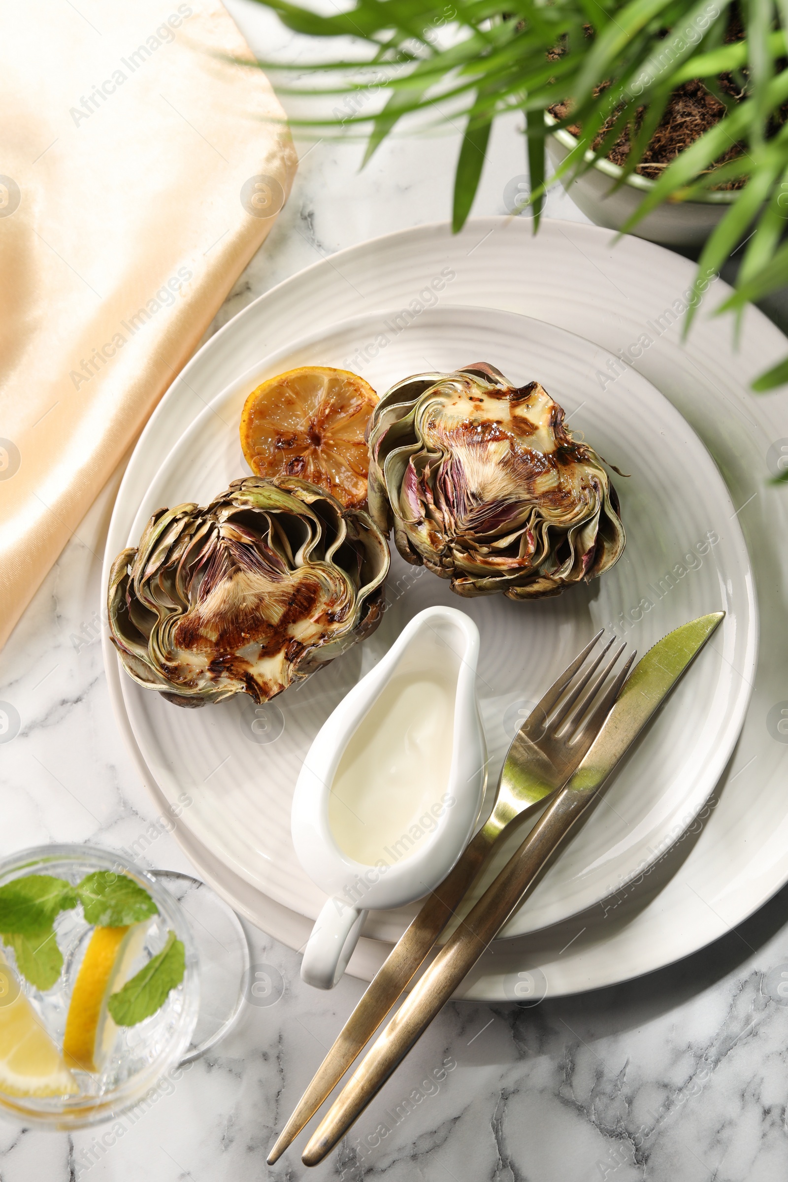 Photo of Tasty grilled artichokes served on white marble table, flat lay