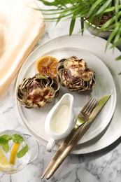 Photo of Tasty grilled artichokes served on white marble table, flat lay
