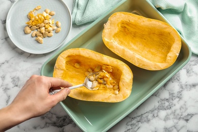 Woman removing seeds from spaghetti squash with spoon on table, top view
