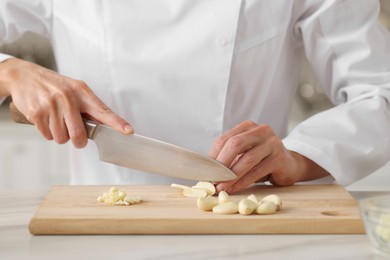 Photo of Professional chef cutting garlic at white marble table indoors, closeup