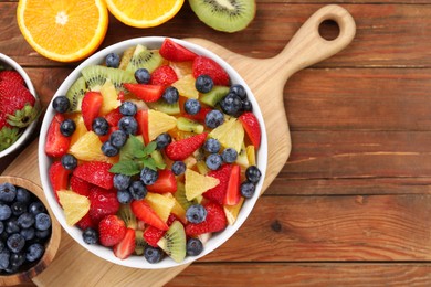 Photo of Delicious fresh fruit salad in bowl and ingredients on wooden table, flat lay. Space for text
