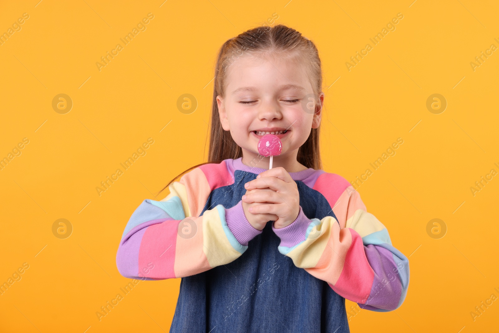 Photo of Happy little girl with lollipop on orange background