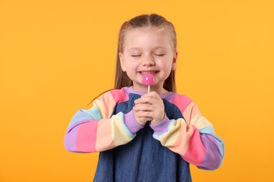 Photo of Happy little girl with lollipop on orange background