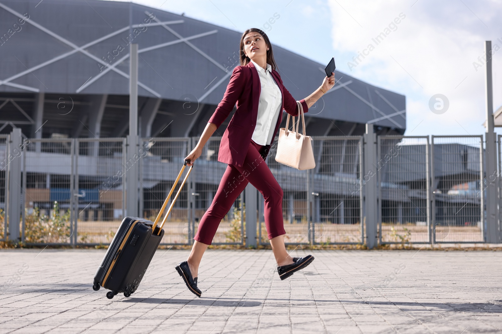 Photo of Being late. Businesswoman with black suitcase and passport running outdoors
