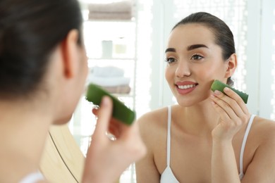 Photo of Young woman with aloe vera leaf near mirror indoors
