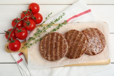 Photo of Tasty grilled hamburger patties, cherry tomatoes and thyme on white wooden table, flat lay