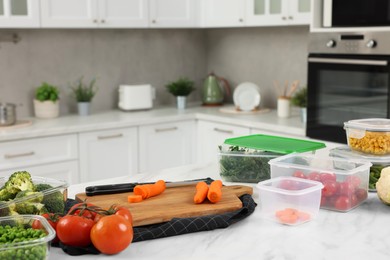 Photo of Containers with different fresh products, board and knife on white marble table in kitchen, space for text. Food storage
