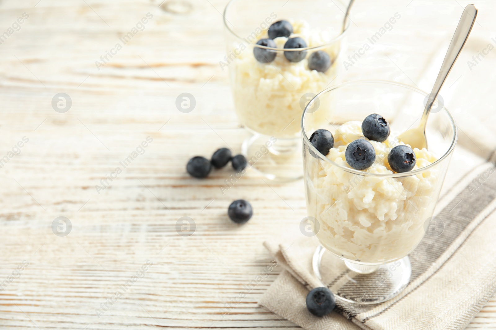 Photo of Creamy rice pudding with blueberries in dessert bowls on white wooden table. Space for text