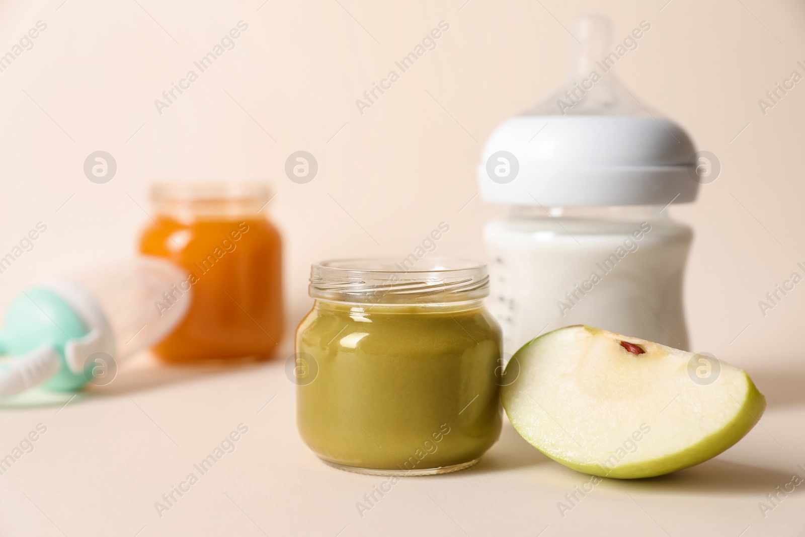 Photo of Jar with healthy baby food, bottle of milk and apple on beige background. Space for text