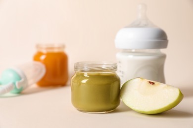 Photo of Jar with healthy baby food, bottle of milk and apple on beige background. Space for text