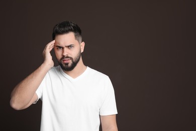 Photo of Young man suffering from headache on dark background, space for text