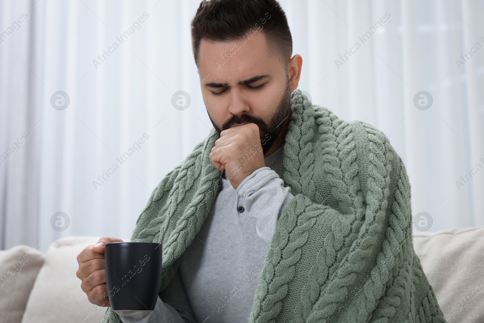Photo of Sick man with cup coughing at home