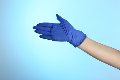 Photo of Woman in latex gloves on light blue background, closeup of hand