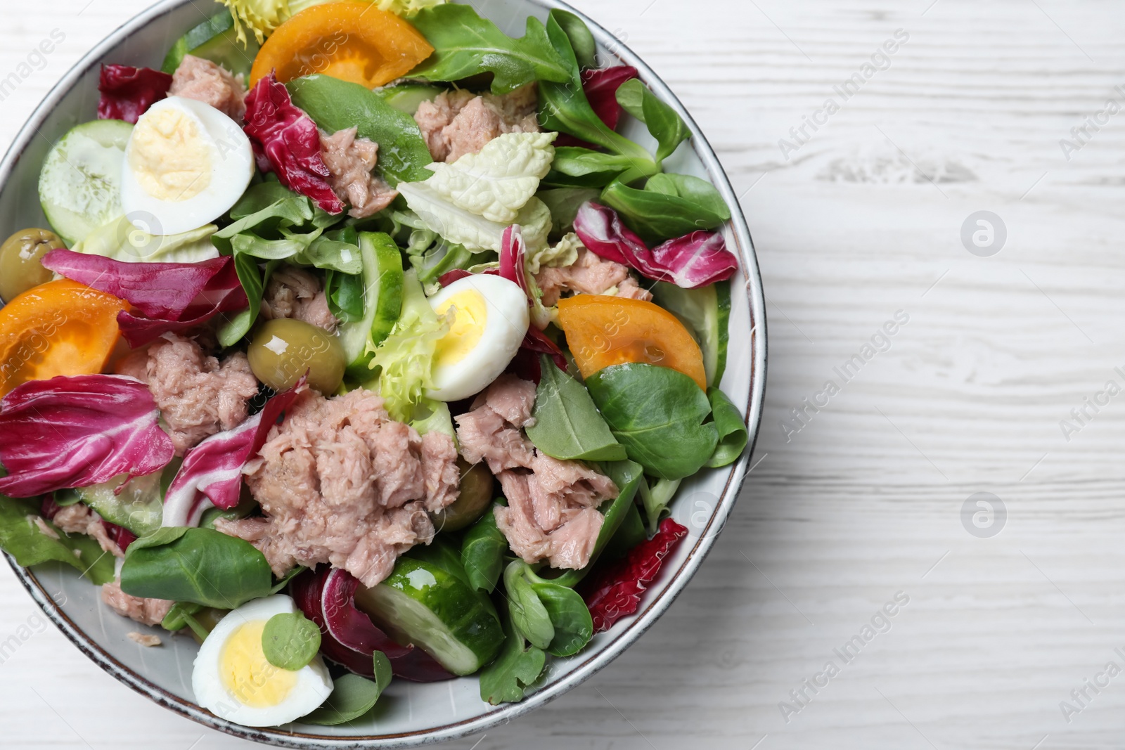 Photo of Bowl of delicious salad with canned tuna and vegetables on white wooden table, top view