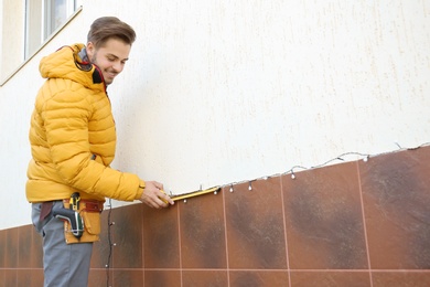 Young man measuring outdoor wall while hanging Christmas lights