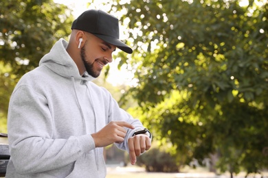 Photo of Young man with wireless headphones and smartwatch listening to music in park. Space for text