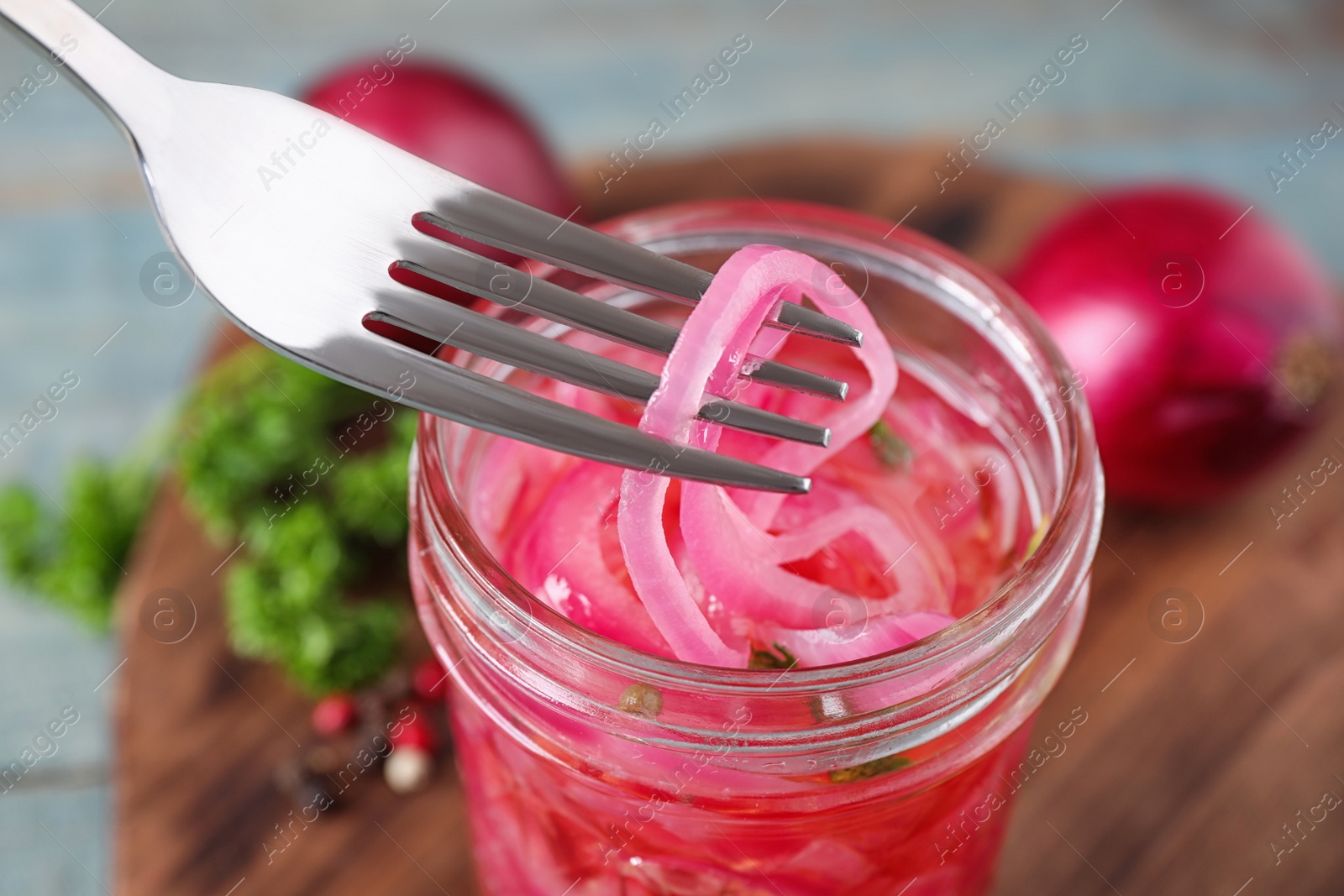 Photo of Fork with tasty pickled onion slices over jar on table, closeup