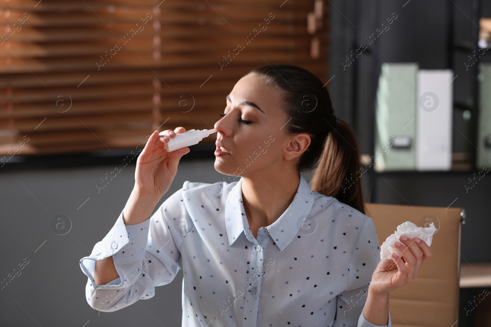 Photo of Ill businesswoman using nasal spray in office