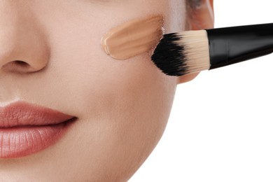 Woman applying foundation on face with brush against white background, closeup