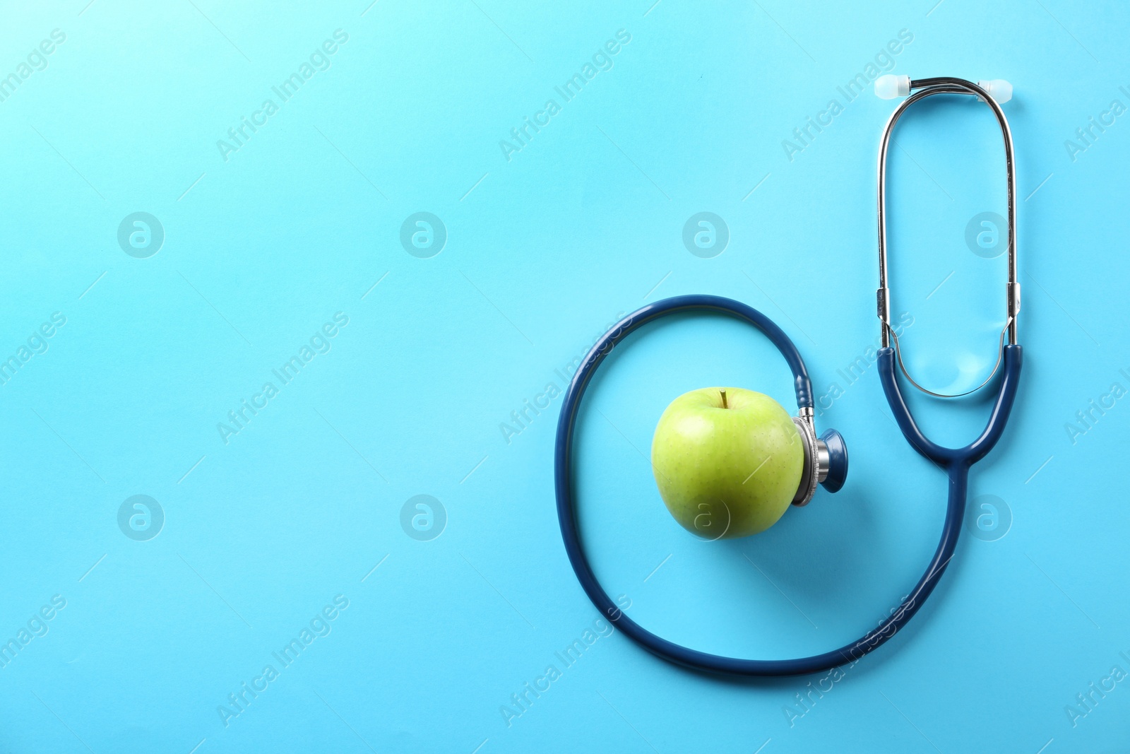 Photo of Flat lay composition with apple and stethoscope on light blue background. Space for text