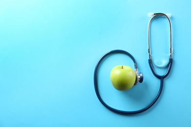 Flat lay composition with apple and stethoscope on light blue background. Space for text