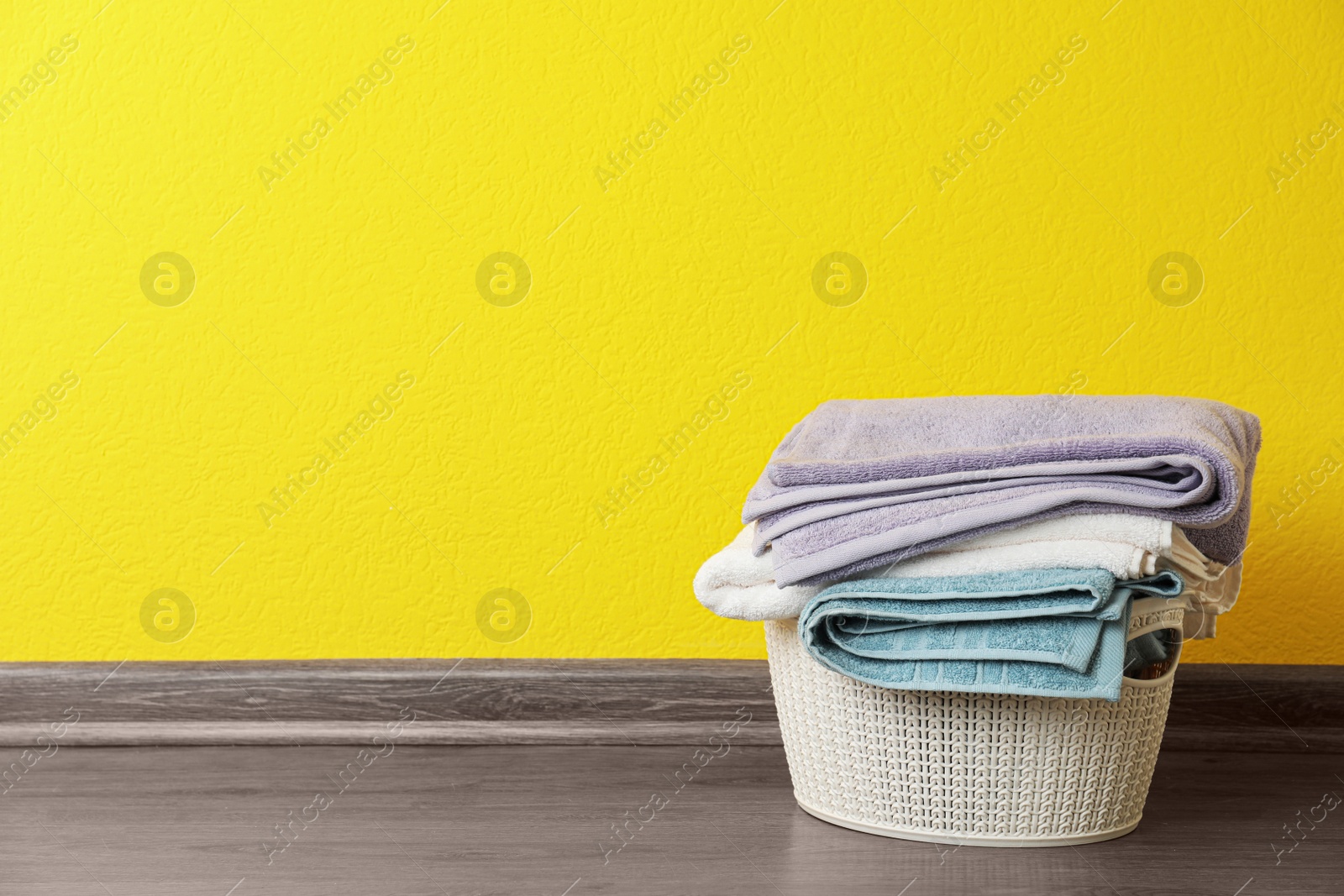 Photo of Basket with clean laundry on floor near yellow wall, space for text