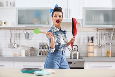 Photo of Funny young housewife with frying pan in kitchen