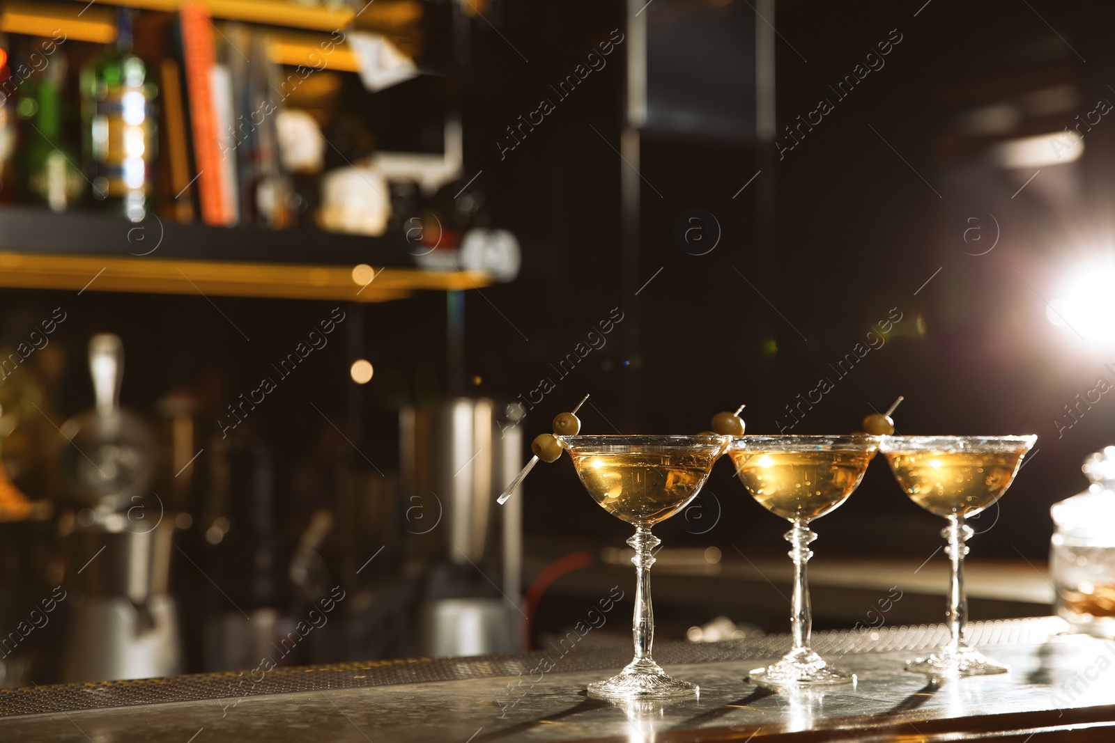 Photo of Glasses of martini cocktail with olives on bar counter. Space for text