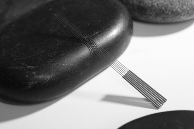 Acupuncture needles and spa stones on white table, closeup