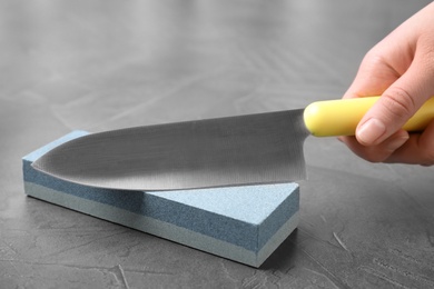 Woman sharping chef's knife at grey table, closeup