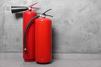 Red fire extinguishers near grey wall, space for text
