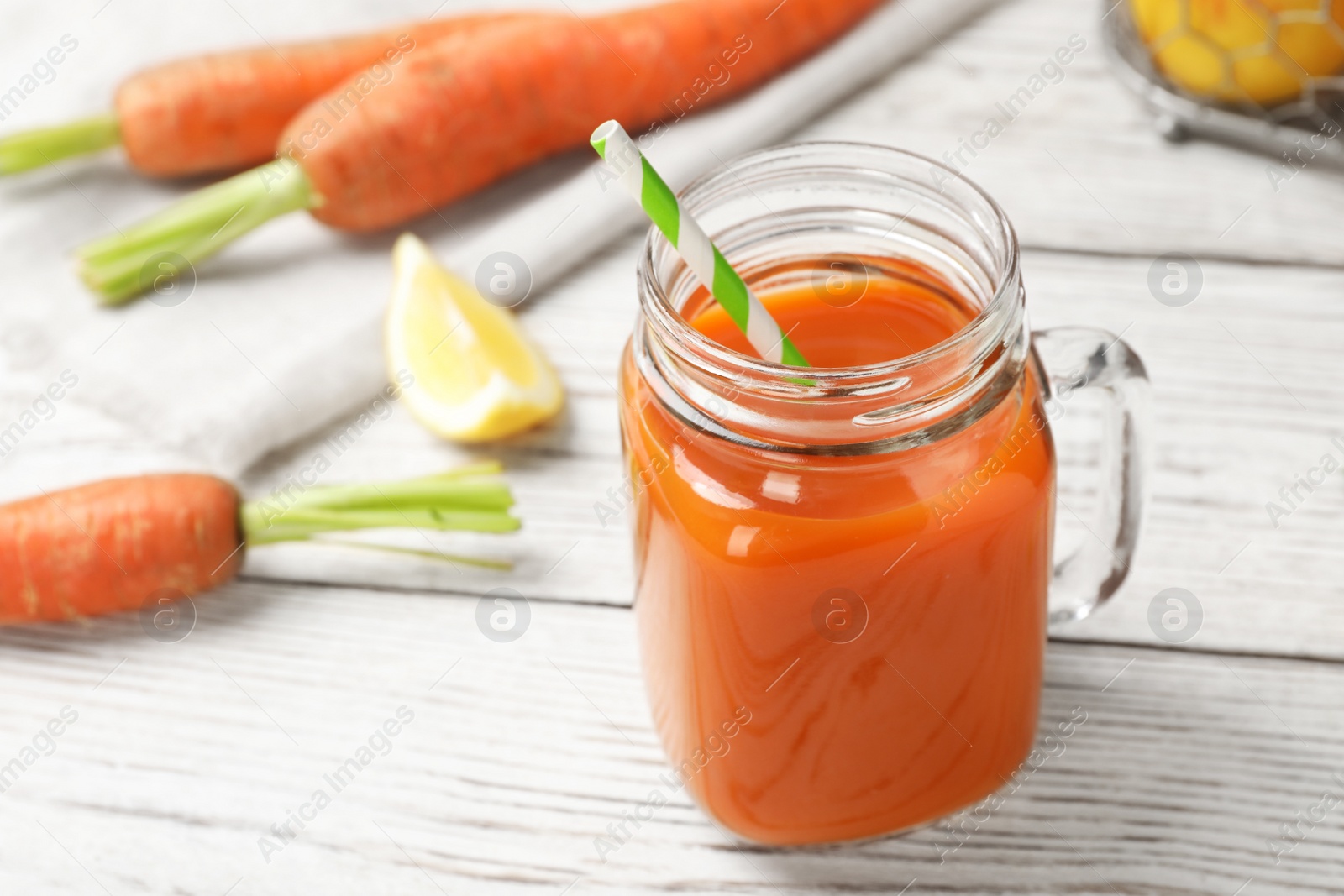 Photo of Mason jar with fresh carrot juice on white wooden table, space for text