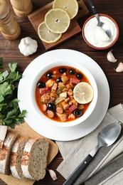 Photo of Meat solyanka soup with sausages, olives and vegetables served on wooden table, flat lay