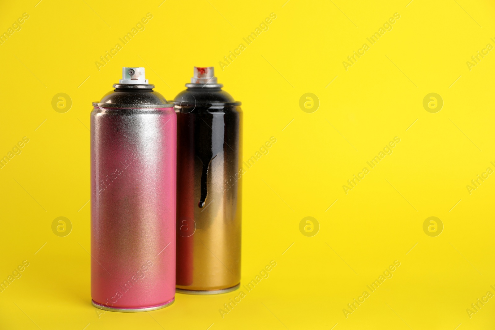 Photo of Used cans of spray paints on yellow background. Space for text