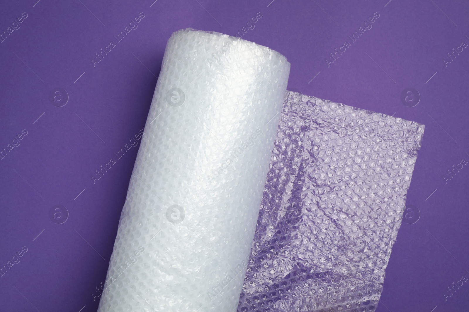 Photo of Bubble wrap roll on purple background, top view