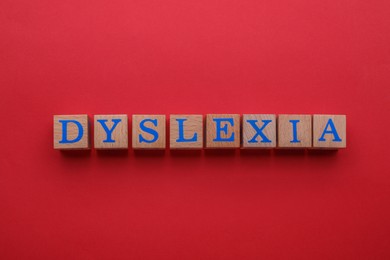 Wooden cubes with word Dyslexia on red background, flat lay