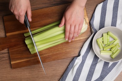 Woman cutting fresh green celery at wooden table, top view