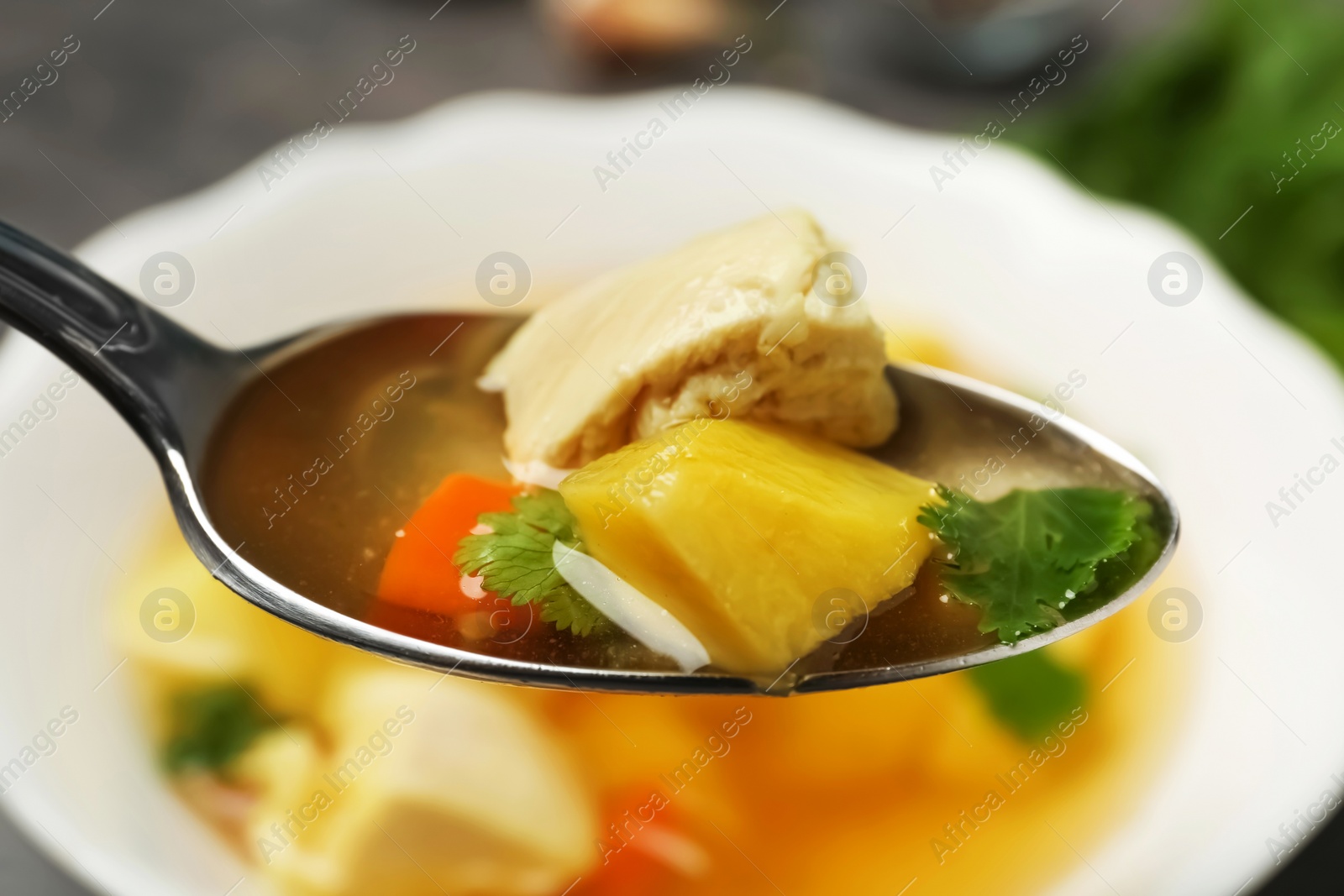 Photo of Spoon with fresh homemade chicken soup on blurred background, closeup