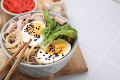 Photo of Bowl of delicious ramen with meat and egg on white tiled table, closeup with space for text. Noodle soup