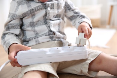 Photo of Little child playing with power strip and plug on floor indoors, closeup. Dangerous situation