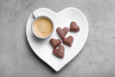 Photo of Cup of coffee and chocolate candies on grey table, top view. Valentine's day breakfast