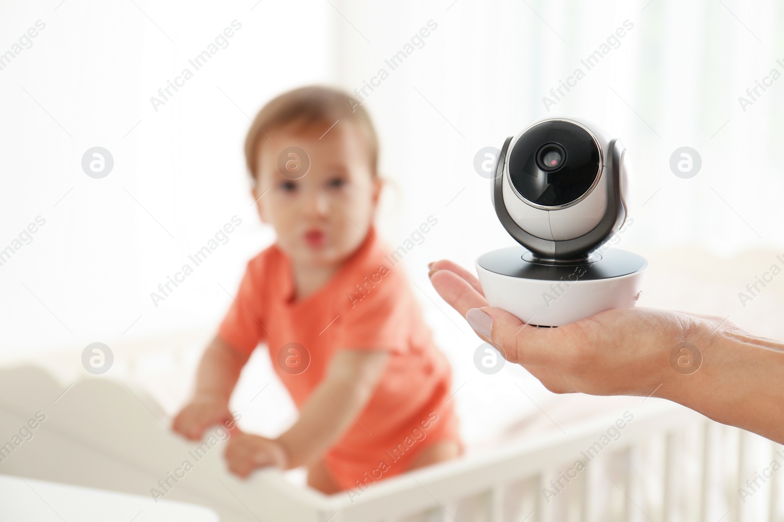 Photo of Woman holding baby camera near crib with child in room. Video nanny