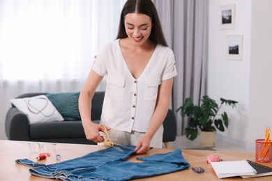 Photo of Happy woman making ripped jeans at table indoors