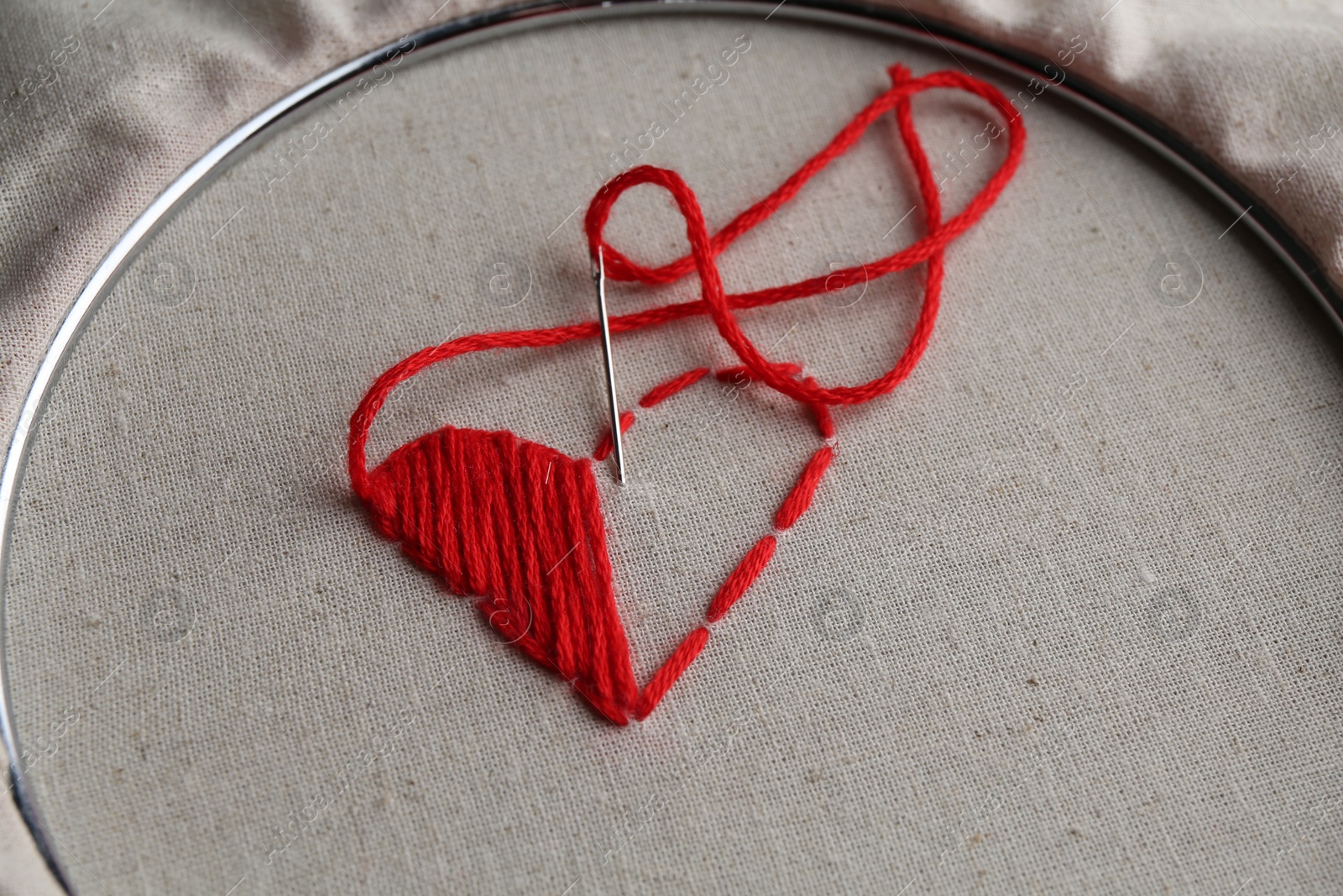 Photo of Embroidered red heart and needle on light cloth, closeup